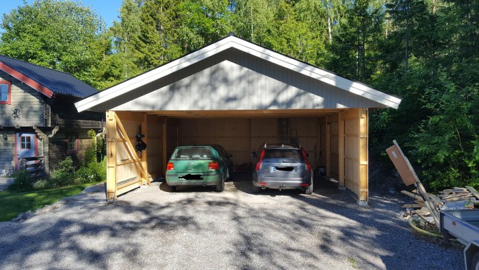 Nyligen byggd carport med två parkerade bilar och rymligt taköverhäng, omgivet av grönska.