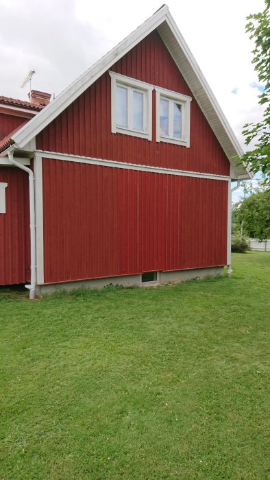 Rödmålat trähus med vita fönsterkarmar, utan presenning på gaveln, på en gräsmatta.