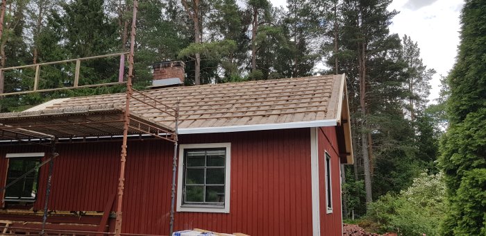 Tak under renovering med borttagna pannor, uppbyggd ställning och omgivande grönska.