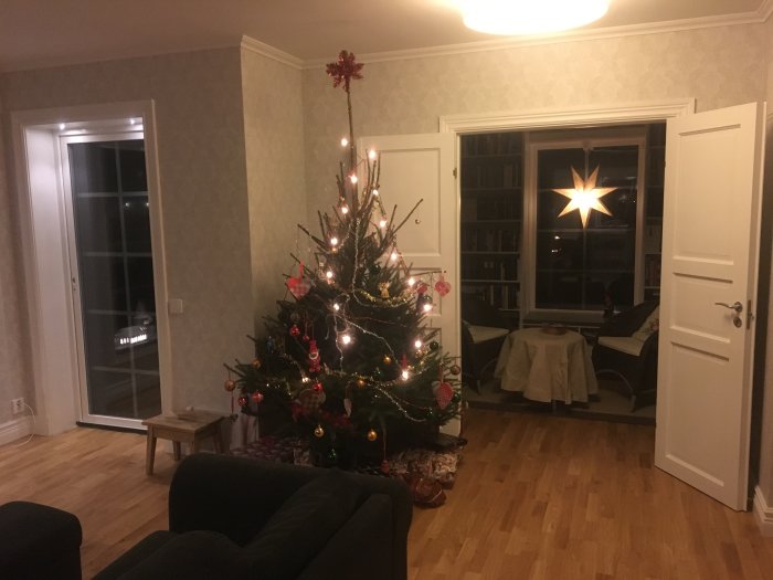 Ett vardagsrum med julgran, bokhylla och tapetserade väggar, inrett efter renovering.