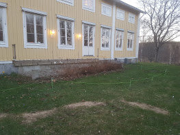 Plats där en gammal altan rivits, synliga bärlinor och betongplintar vid husgrund på en trädgård.