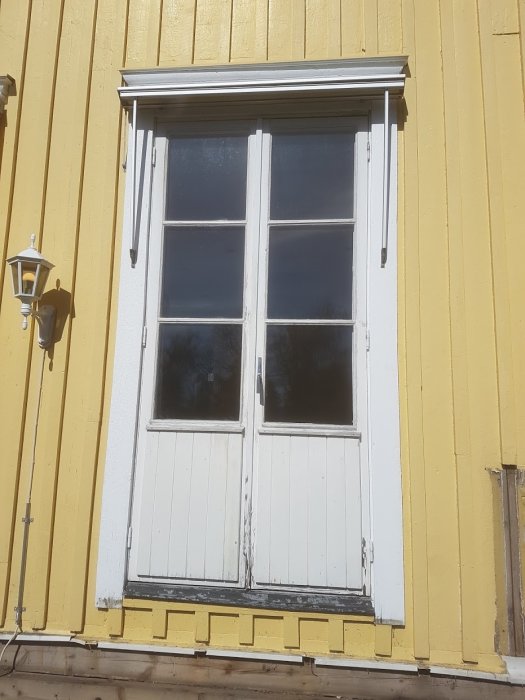 Altandörr i trä på gul husfasad med slitage och behov av utbyte.