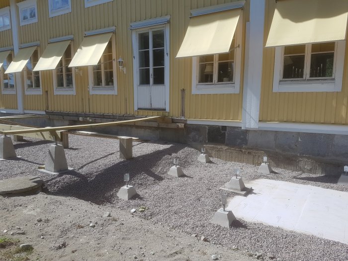 Förberedelseplats för spabad framför gult hus med betongplatta och stödfötter på grus.