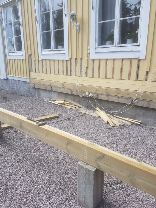 Altanbygge vid husfasad med kapade fasadbrädor och nytt liggande virke för trallmontering.