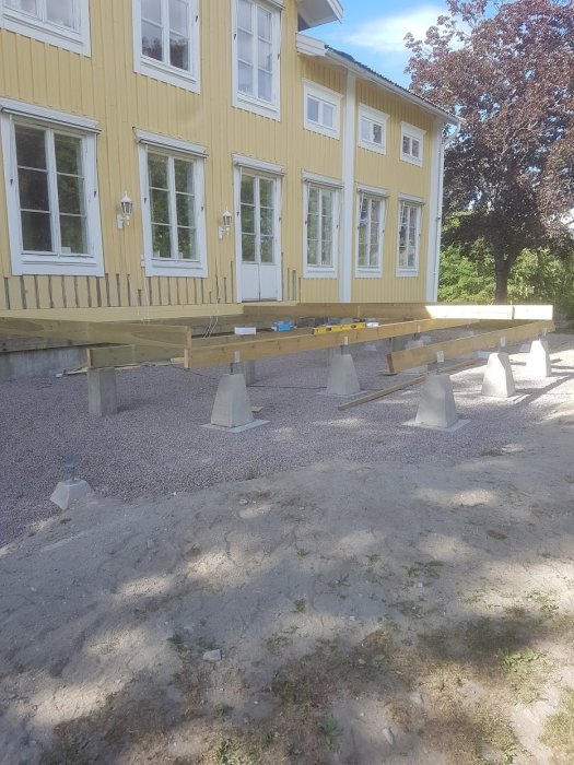 Installation av nya bärlinor under ett gult trähus i byggprocess.
