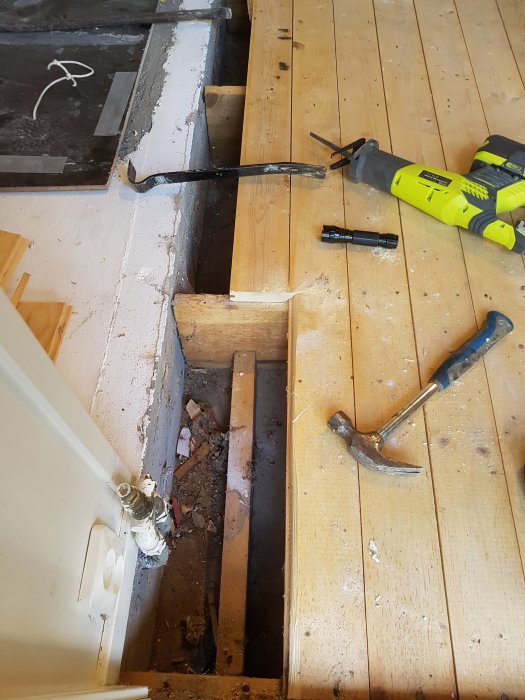 Renoveringsarbete med uppbrutet trägolv och synliga träreglar ovanpå en betongkonstruktion, verktyg synliga.