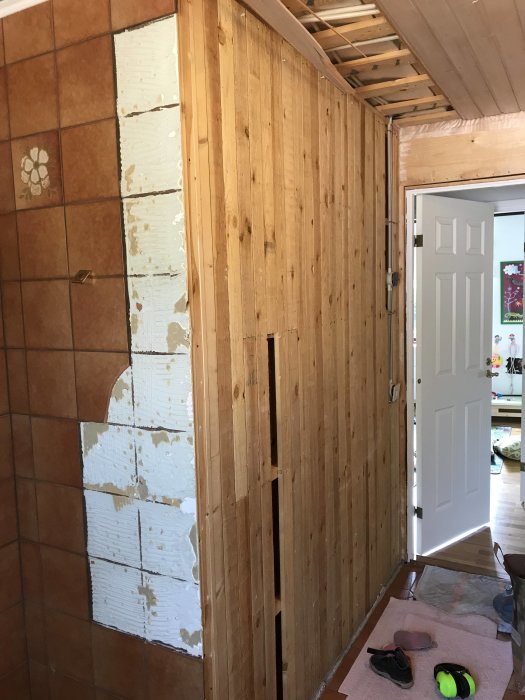 Delvis rivet badrumskakel som avslöjar en underliggande träpanelvägg under pågående renovering.