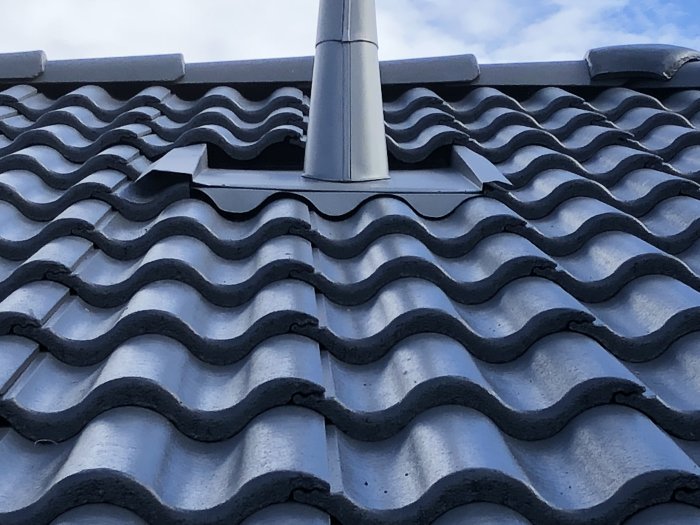 Takpannor med ojämn fasonering kring en ventilationsrör på ett betongtak.