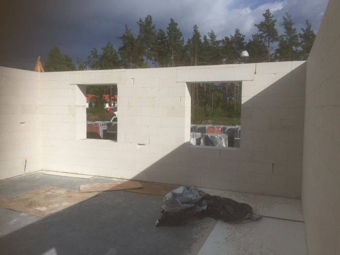 Hus under konstruktion med vit blockmur på balkhöjd och synlig bjälklag i dagsljus.
