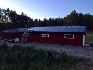 Röd byggnad med paneler under skymning, stegar lutade mot taket.