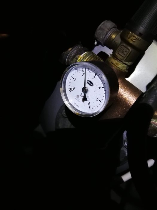 Manometer med nålen nära 4 bar indikerar vattentryck i ett rörsystem, mörk bakgrund.