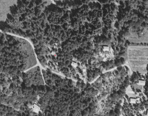 Svartvitt flygfoto från 1971 med röd prick som markerar sydosthörnet av ett hus.