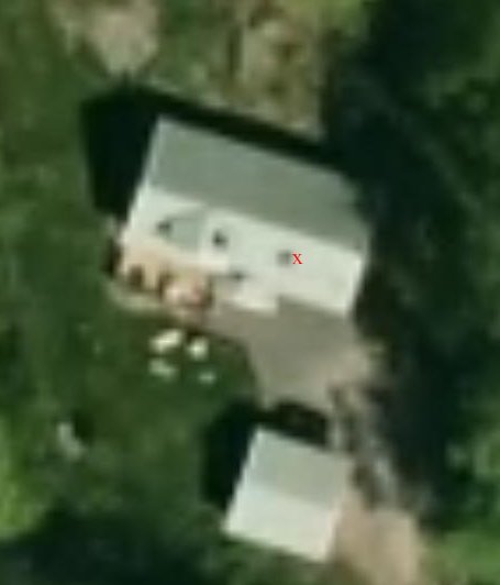 Flygfoto över ett hus med en röd prick markerad vid sydöstra hörnet för att indikera en specifik plats relaterad till en diskussion.