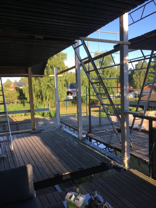 Byggställningar och pågående arbete på en träterrass i solljus.