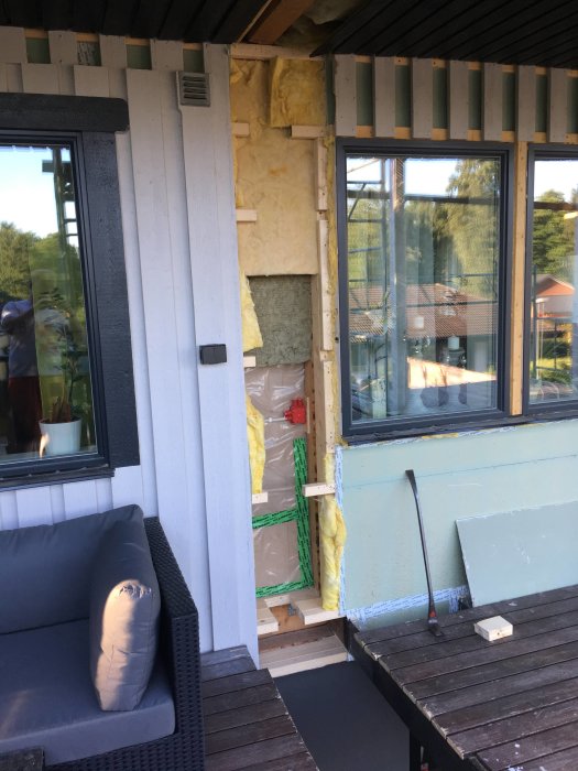 Delvis isolerad uteplats under renovering med synlig mineralullsisolering och oavslutat träarbete.