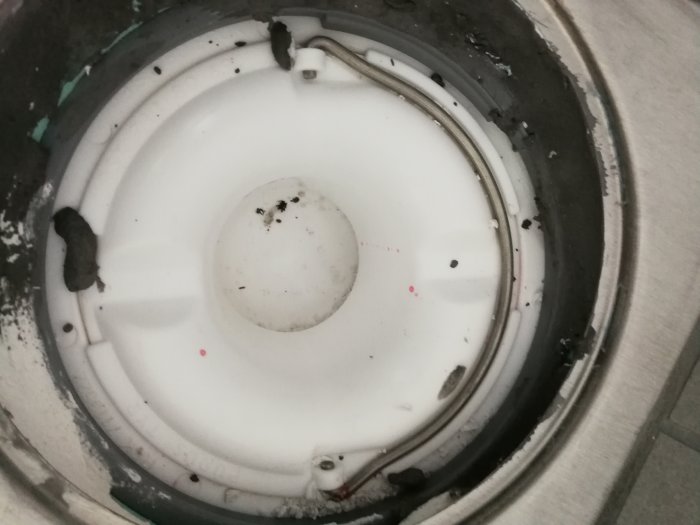 Golvbrunn under konstruktion med synligt vattenlås och föremål som plast och murbruk runt omkring.