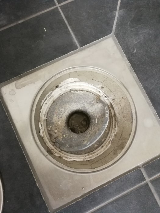 Golvbrunn under konstruktion med synligt vattenlås under klinkerram, omgivet av byggavfall som plast och murbruk.