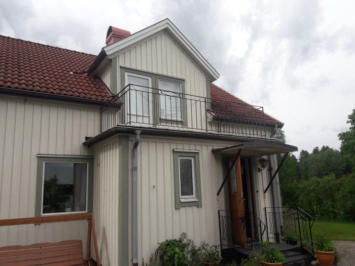 Bild av en husfasad med en balkong försedd med ett järnräcke och frågor om utbyte mot träkonstruktion för att undvika läckage.
