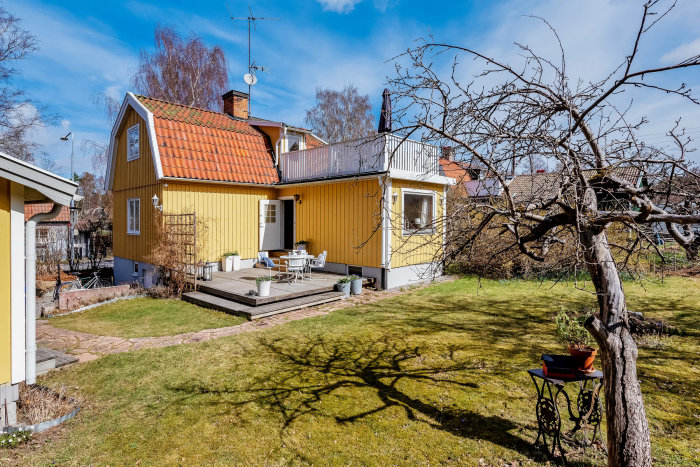 Husets baksida med altan och trädgård i solläge, potentiell plats för ny entré.