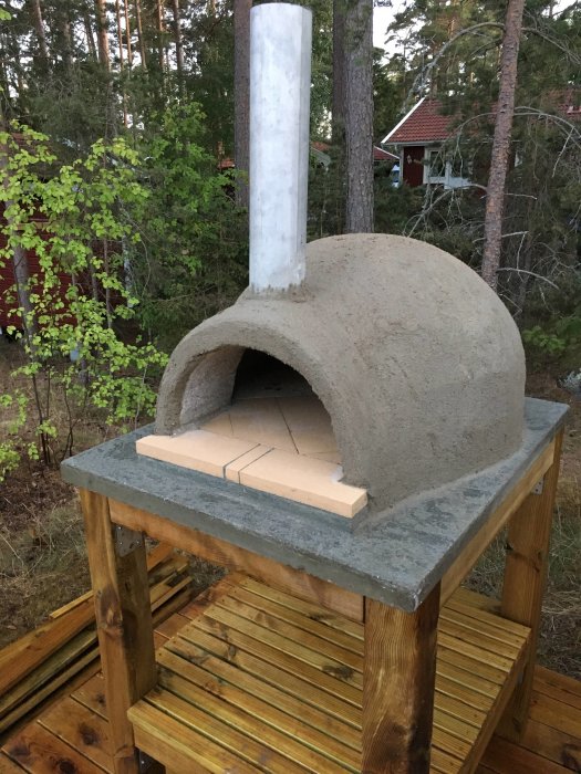 Nybyggd utomhus pizzaugn med putsad yta på trästomme med skorsten, redo för användning.