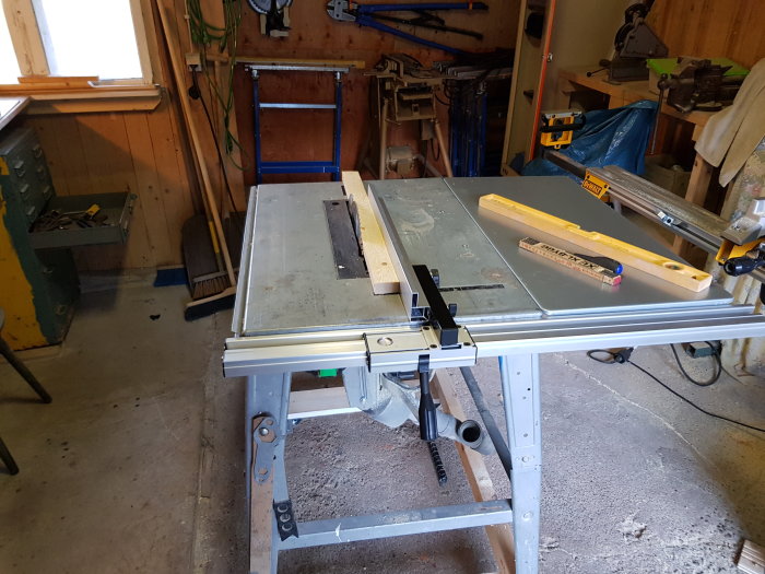 Verkstadsinteriör med en nyinstallerat anhåll på en bordsåg, omgiven av verktyg och arbetsbänkar.