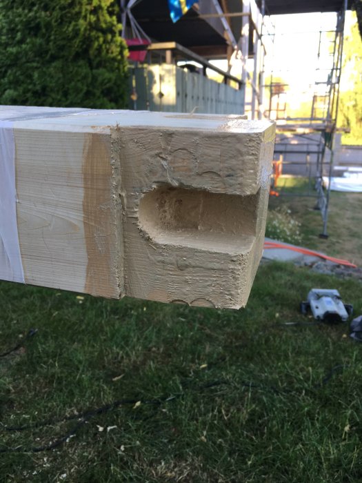Behandlad träplanka med urgröpning hänger framför ett byggarbetsplatsområde utomhus.