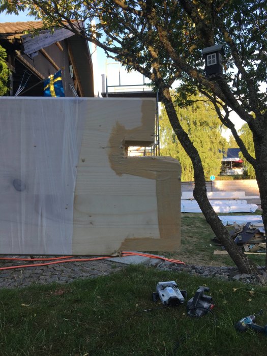 Byggplats med pågående arbete, synlig träskiva och verktyg utspridda på marken.