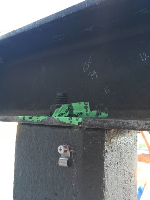 Närbild av en mätlapp fastklämd under en skruv på en svartmålad bjälke under konstruktion.