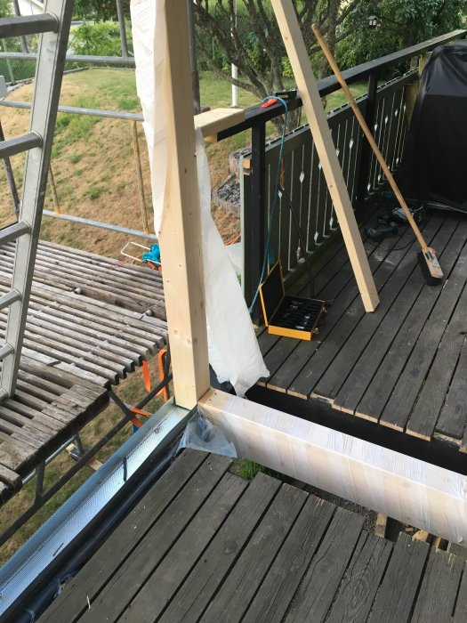 Byggplats med träplankor, verktyg och pågående konstruktion av trästomme på ett däck.