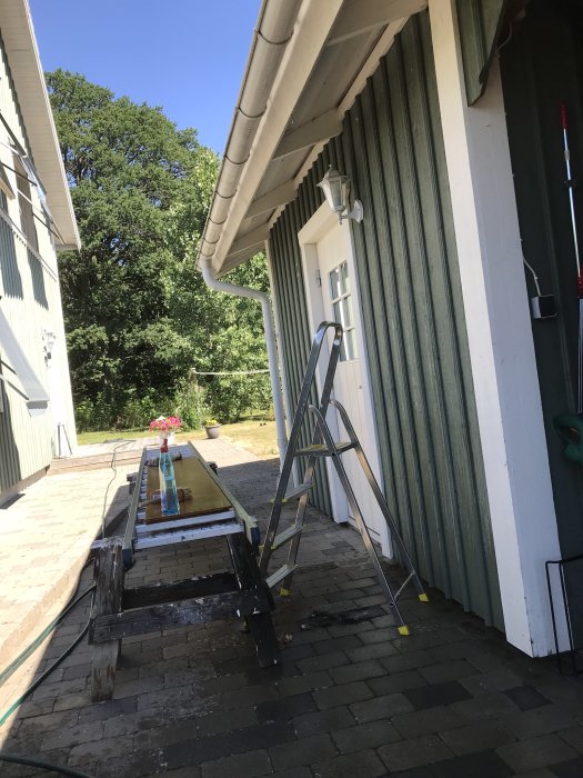 Stege vid en grönvit carport som har tvättats inför målning, med rengöringsverktyg synligt.