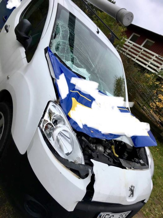 Vit bil med starkt krossad framdel och krossad vindruta står parkerad.