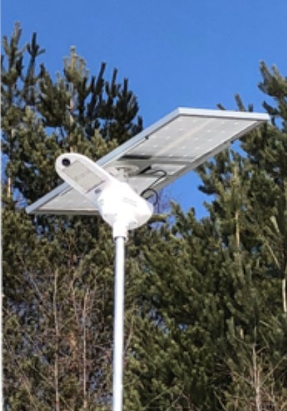 Solpanel monterad på stolpe framför träd med klarblå himmel i bakgrunden.
