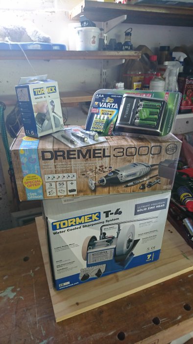 Verktyg och tillbehör på en arbetsbänk, inklusive Tormek T4 slipmaskin, Dremel 3000 och Varta batteriladdare.