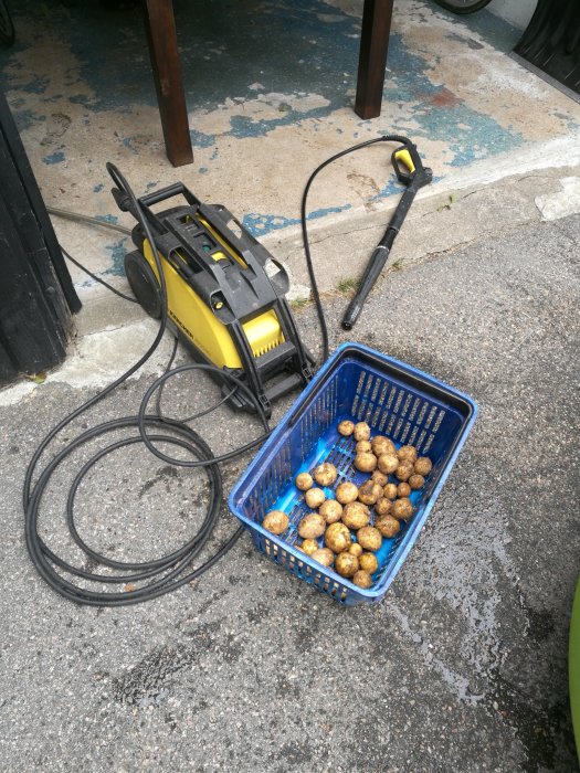 Högtryckstvätt bredvid blå korg med skalade potatisar på en uppfart.