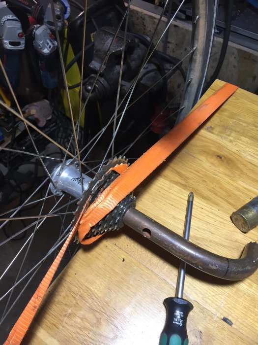 Cykelhjul i ett verktygsfyllt garage med ett improviserat verktyg användandes ett kopparrör och rem för att byta eker.