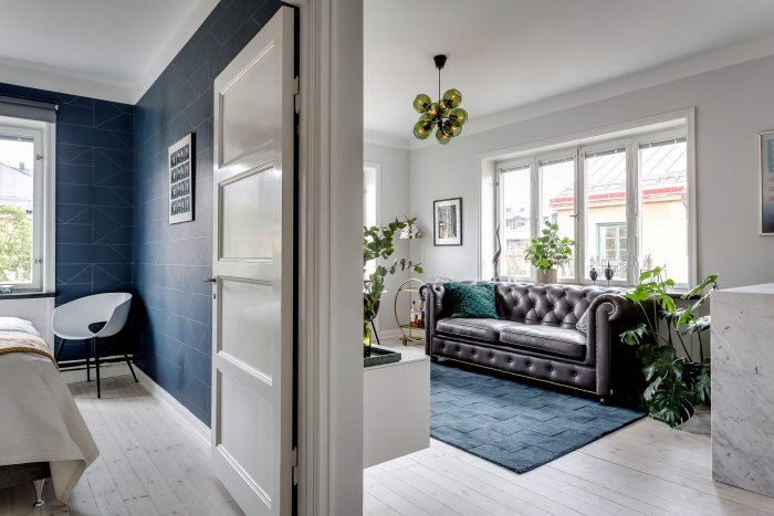 Elegant 30-talslägenhet med vita golvsocklar, mönstrad blå vägg och chesterfieldsoffa.