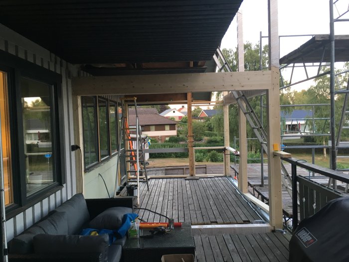Byggprojekt med limträ monterat i stålbalk på en veranda under konstruktion, med arbetsmaterial synligt.