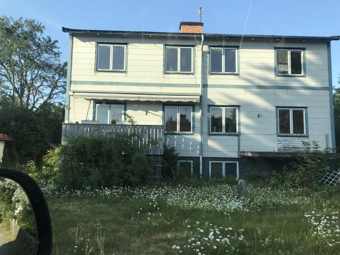 Ett tvåvånings renoveringsobjekt av en villa med synliga skador och omgiven av en övervuxen trädgård.