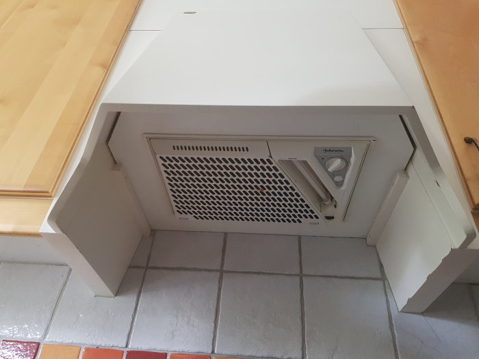 En vit kökskåpa av mdf-material med en inbyggd köksfläkt ovanför en kaklad bänkskiva.