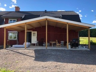 Röd trävilla med svart tak och en nybyggd veranda med tak och utemöbler.