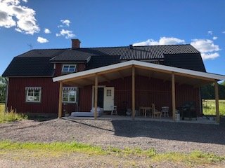 Rödmålat trähus med svart tak och öppen veranda under en klarblå himmel.