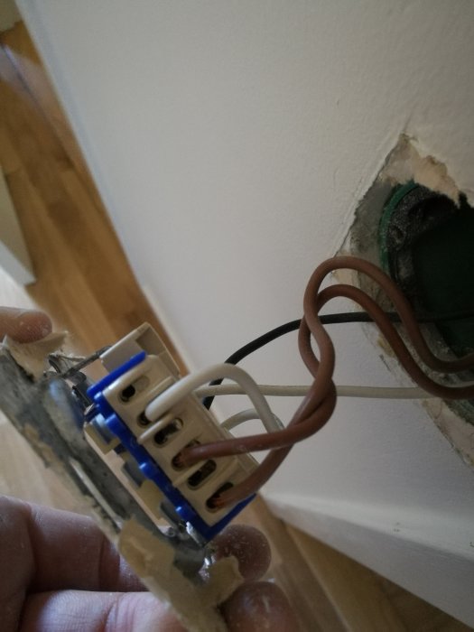 Elektrisk dosa i vägg med exponerade kablar, en vit kabel är kopplad tvärs över dosan.