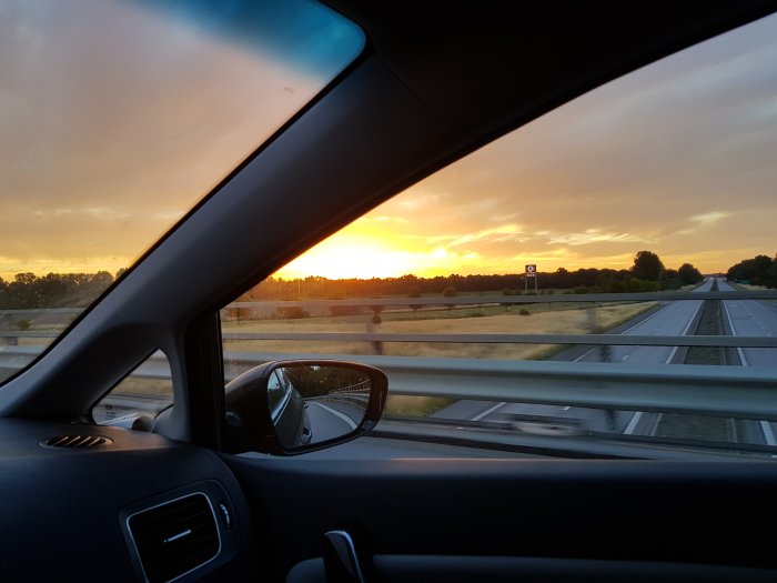 Solnedgång sett från bilens passagerarsida med öppet fönster på motorväg.