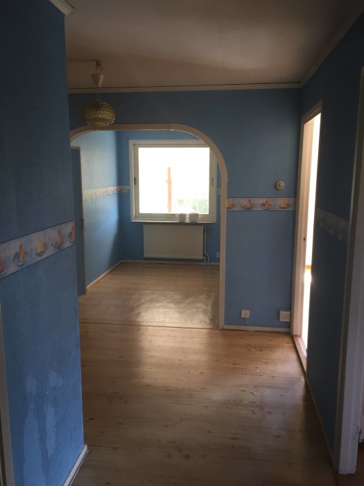 Interiör av ett hus före renovering med blåa väggar, trägolv och en bågformad öppning mellan rum.