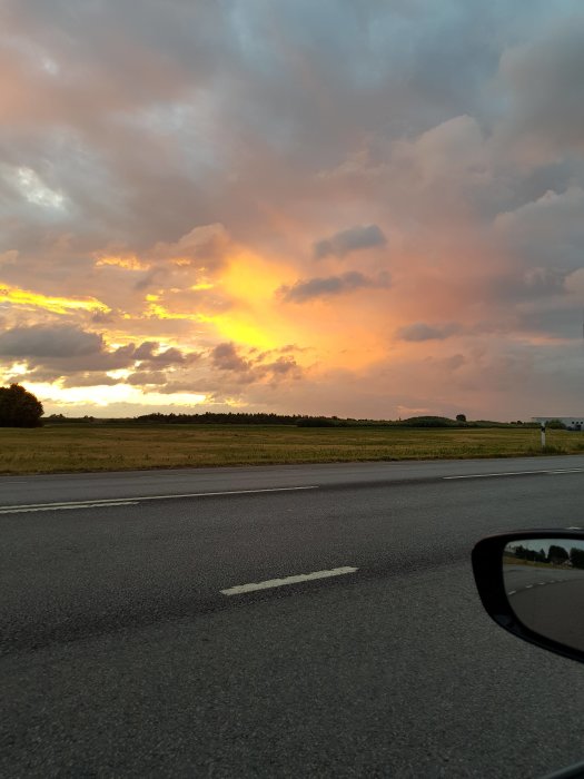 Dramatisk solnedgång med orange färgtoner sett från bil vid vägkanten.