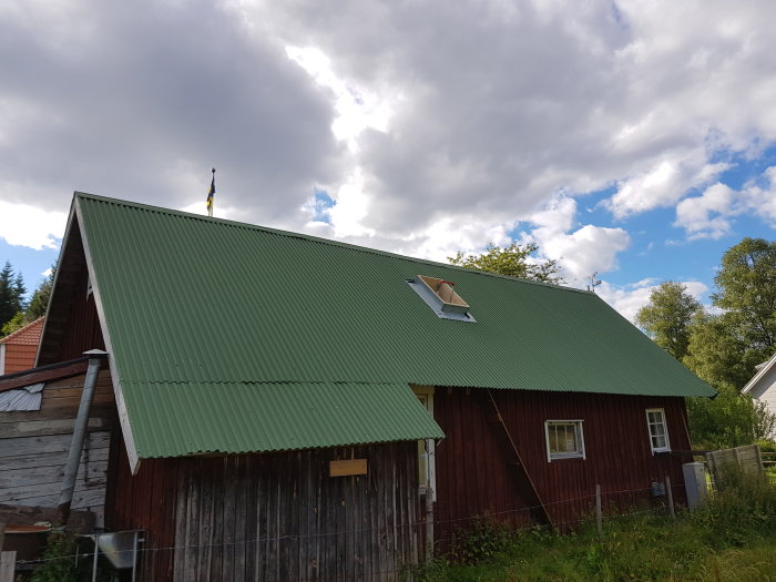 Röd snickarbod med grönt tak och en nyöppnad lucka för sotare under en molnig himmel.