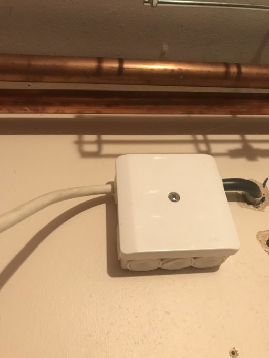 Vit kopplingsdosa med elektrisk kabel på vägg under kopparledning.