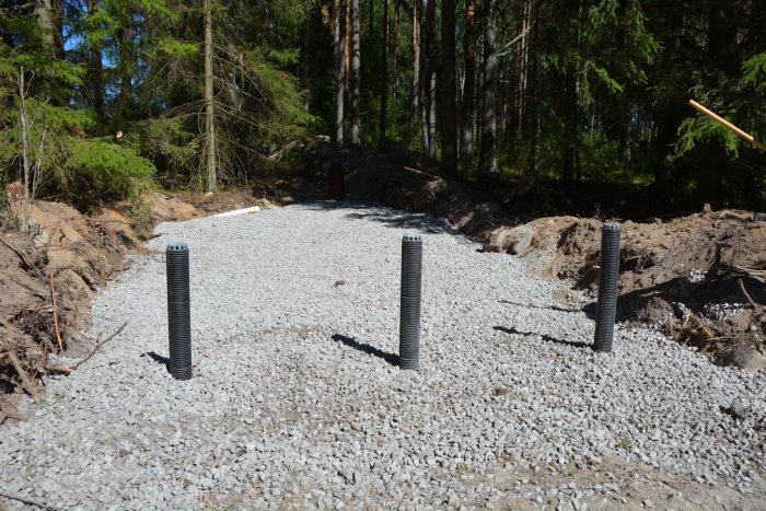 Nyinstallerad infiltration för avlopp med grus och synliga ventiler på en byggplats i skogsmiljö.