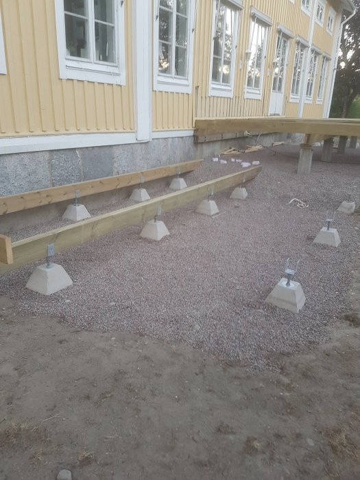 Ramverket för ett lägre trädäck i byggfas utan räcke bredvid ett gult hus med stengrund.