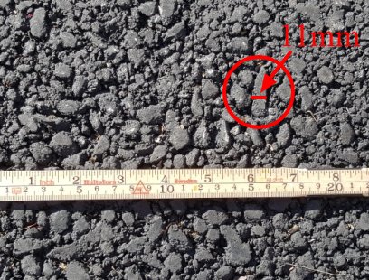 Måttband bredvid asfaltstenar med en markerad sten som mäter 11 mm.